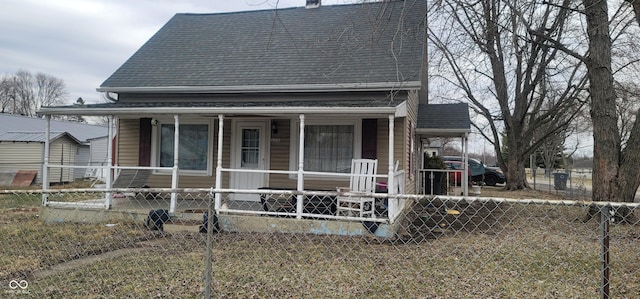 rear view of property with a shingled roof, a fenced front yard, a chimney, covered porch, and a carport