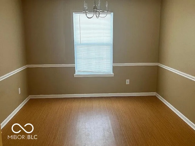 empty room featuring a notable chandelier, baseboards, and wood finished floors