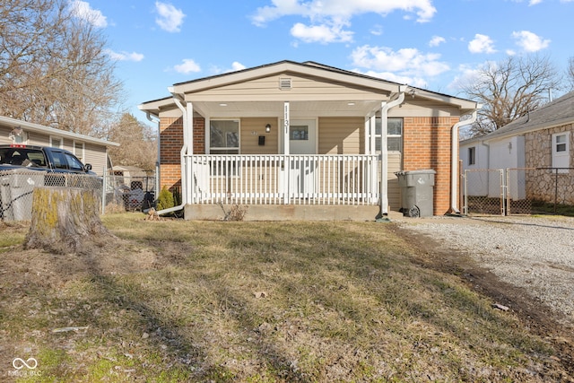 view of front of property featuring a front lawn, fence, a porch, and brick siding