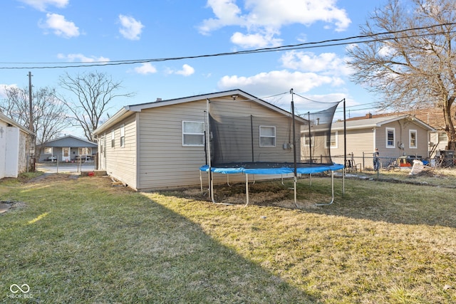 rear view of house with a trampoline, fence, and a lawn