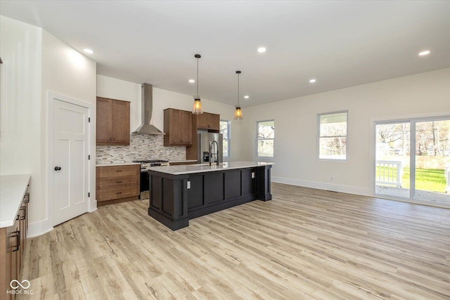 kitchen featuring light wood-style flooring, stainless steel appliances, light countertops, wall chimney range hood, and backsplash