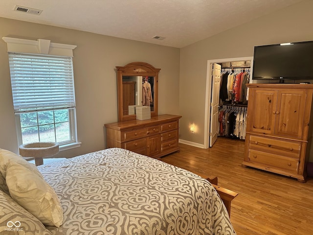 bedroom featuring visible vents, a walk in closet, lofted ceiling, light wood-style floors, and a closet