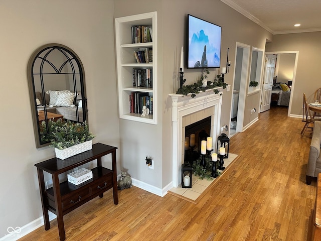 living area featuring built in shelves, a tiled fireplace, wood finished floors, crown molding, and baseboards