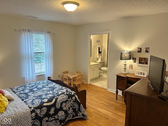 bedroom with visible vents, a textured ceiling, ensuite bath, light wood finished floors, and baseboards