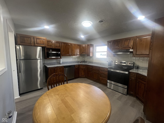 kitchen featuring under cabinet range hood, backsplash, light wood-type flooring, and appliances with stainless steel finishes