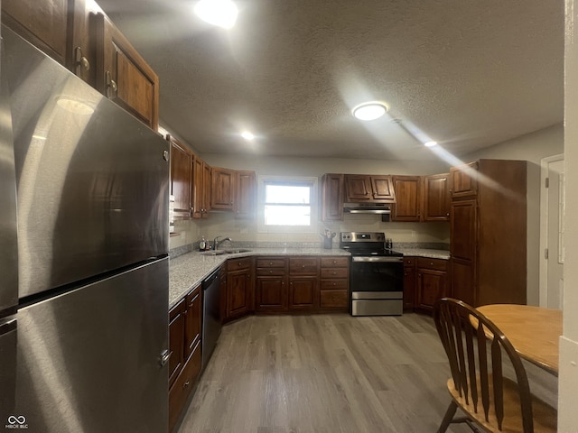 kitchen with under cabinet range hood, a sink, light wood-style floors, appliances with stainless steel finishes, and light countertops