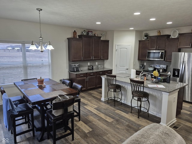 kitchen featuring dark brown cabinetry, appliances with stainless steel finishes, an island with sink, and dark wood-type flooring