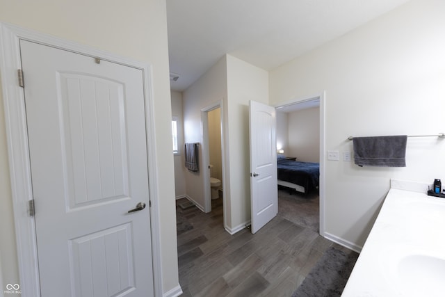 bathroom with baseboards, toilet, double vanity, wood finished floors, and a sink