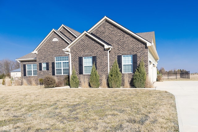 view of front of house with driveway, brick siding, a front yard, and fence