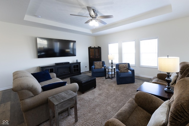 living area with a tray ceiling, a ceiling fan, and baseboards