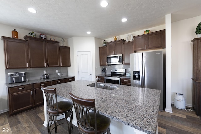 kitchen with tasteful backsplash, dark wood-type flooring, dark brown cabinetry, stainless steel appliances, and a sink