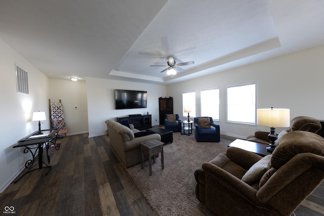 living area with visible vents, a ceiling fan, a tray ceiling, dark wood-style floors, and baseboards