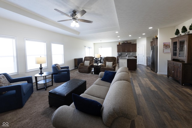 living room with a tray ceiling, plenty of natural light, baseboards, and dark wood-style floors