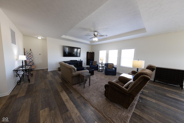 living room with dark wood-style floors, visible vents, a textured ceiling, and a tray ceiling