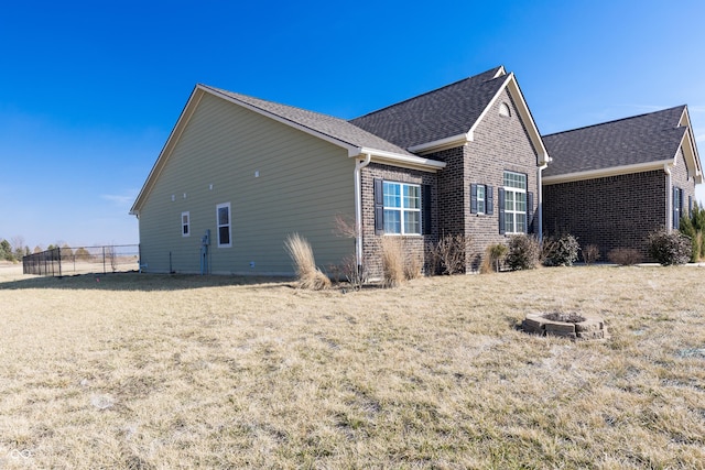 view of side of home with brick siding, an outdoor fire pit, a lawn, and fence