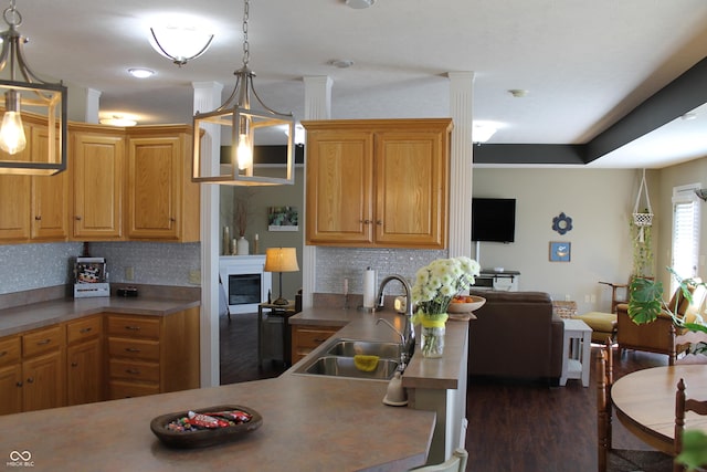 kitchen with dark wood-style floors, decorative light fixtures, a sink, a fireplace, and backsplash