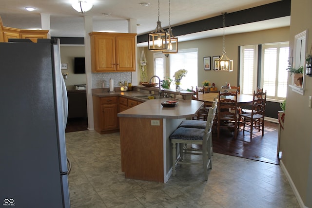 kitchen with decorative backsplash, a kitchen breakfast bar, freestanding refrigerator, a peninsula, and a sink