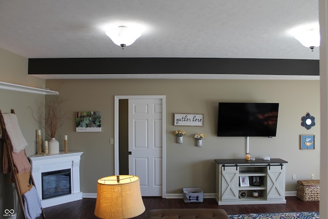 living area with dark wood-type flooring, a glass covered fireplace, and baseboards