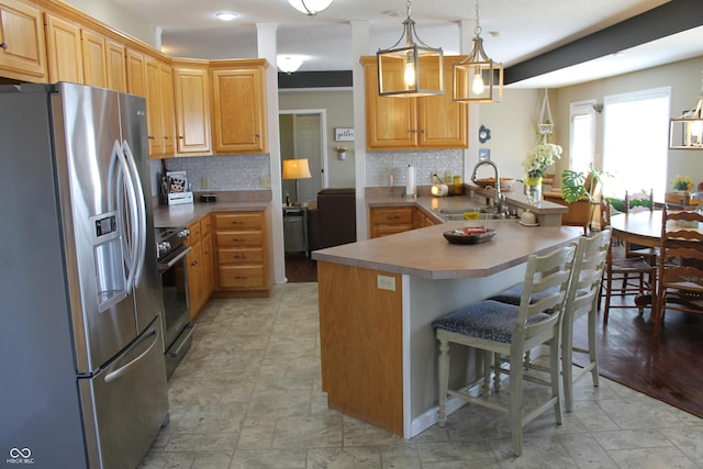 kitchen featuring a breakfast bar area, a peninsula, a sink, appliances with stainless steel finishes, and tasteful backsplash