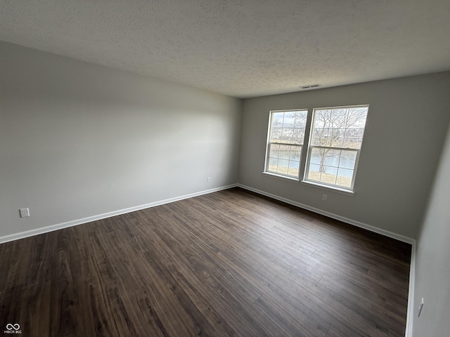 spare room featuring dark wood-type flooring, visible vents, a textured ceiling, and baseboards