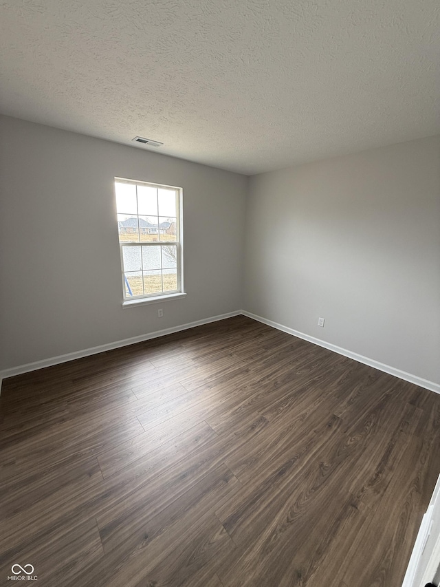 unfurnished room featuring visible vents, dark wood finished floors, a textured ceiling, and baseboards