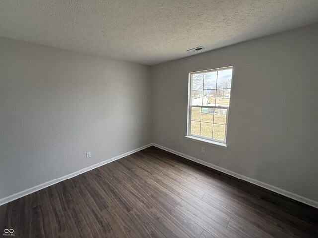 spare room featuring a textured ceiling, dark wood finished floors, visible vents, and baseboards