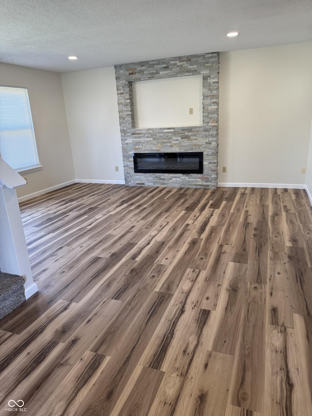 unfurnished living room featuring baseboards, a stone fireplace, a textured ceiling, and wood finished floors