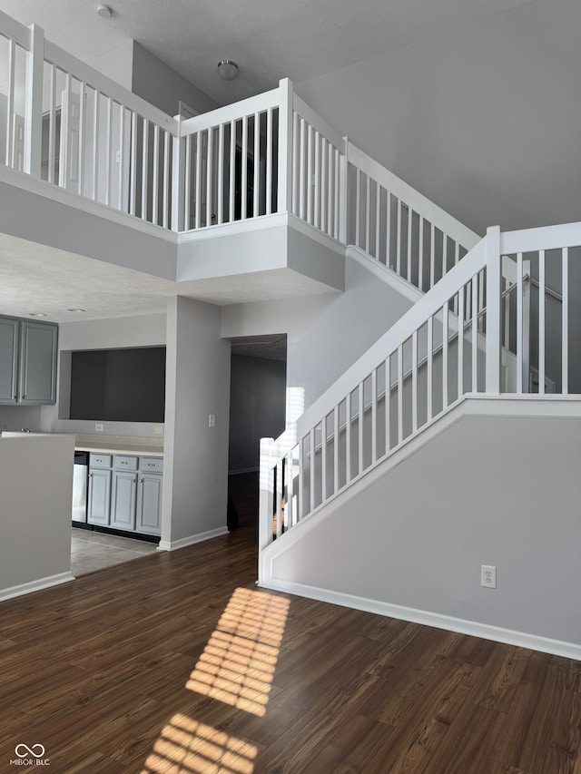 stairway with baseboards, a towering ceiling, and wood finished floors