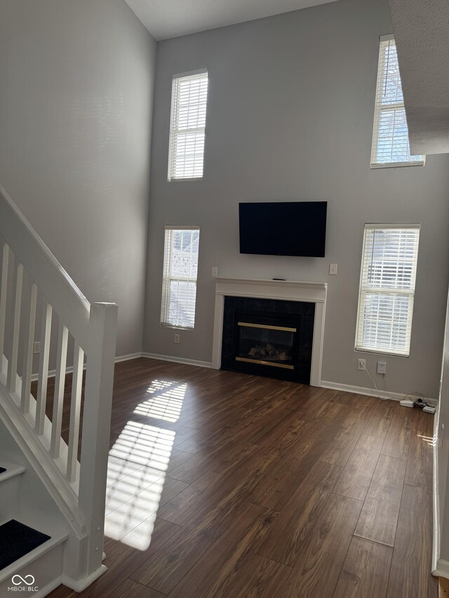 unfurnished living room featuring stairway, wood finished floors, baseboards, a towering ceiling, and a glass covered fireplace