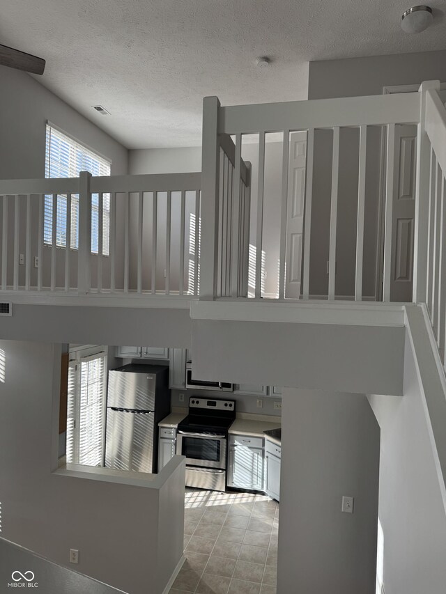 kitchen with visible vents, light tile patterned flooring, appliances with stainless steel finishes, a textured ceiling, and a towering ceiling