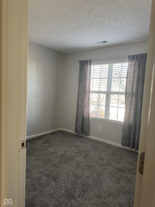 carpeted spare room featuring visible vents, a textured ceiling, and baseboards