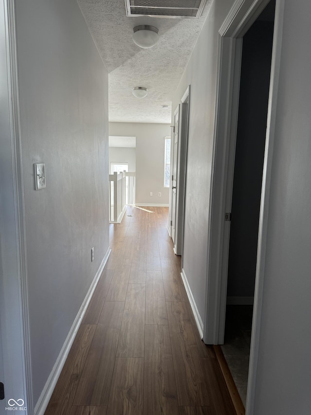 hallway featuring dark wood-type flooring, baseboards, visible vents, and a textured ceiling