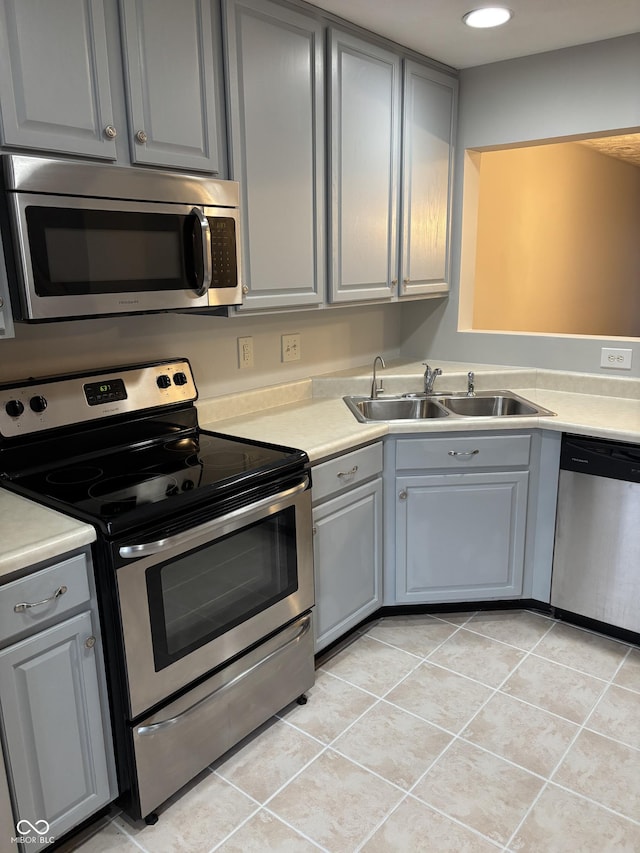 kitchen with a sink, light tile patterned flooring, appliances with stainless steel finishes, and gray cabinetry