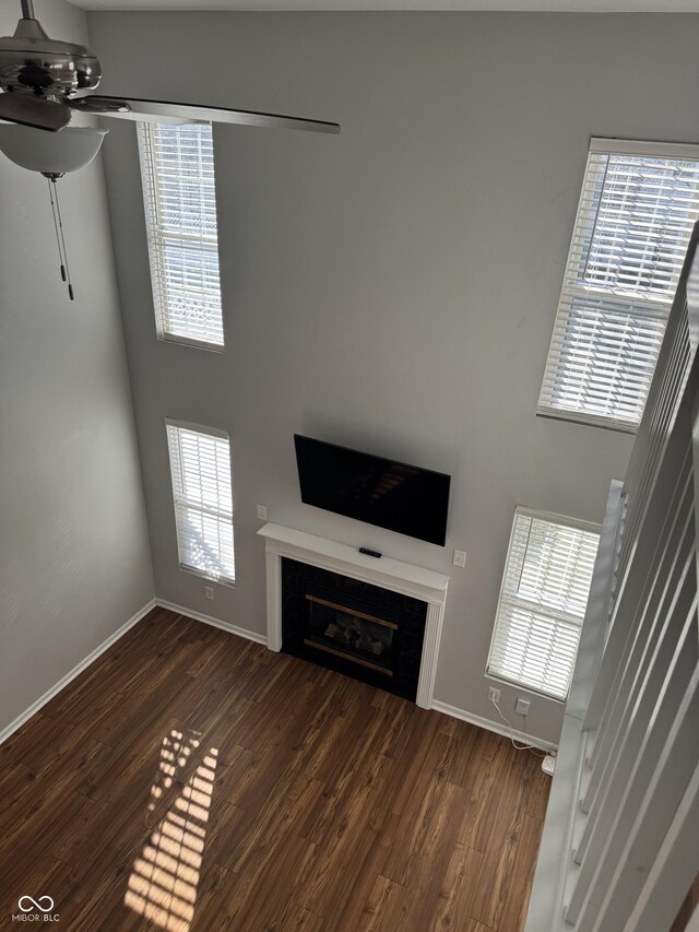 unfurnished living room featuring a glass covered fireplace, wood finished floors, baseboards, and ceiling fan