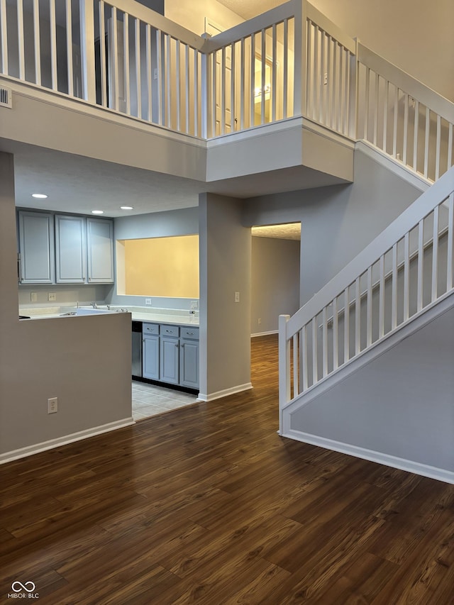 unfurnished living room with stairway, wood finished floors, baseboards, and a towering ceiling