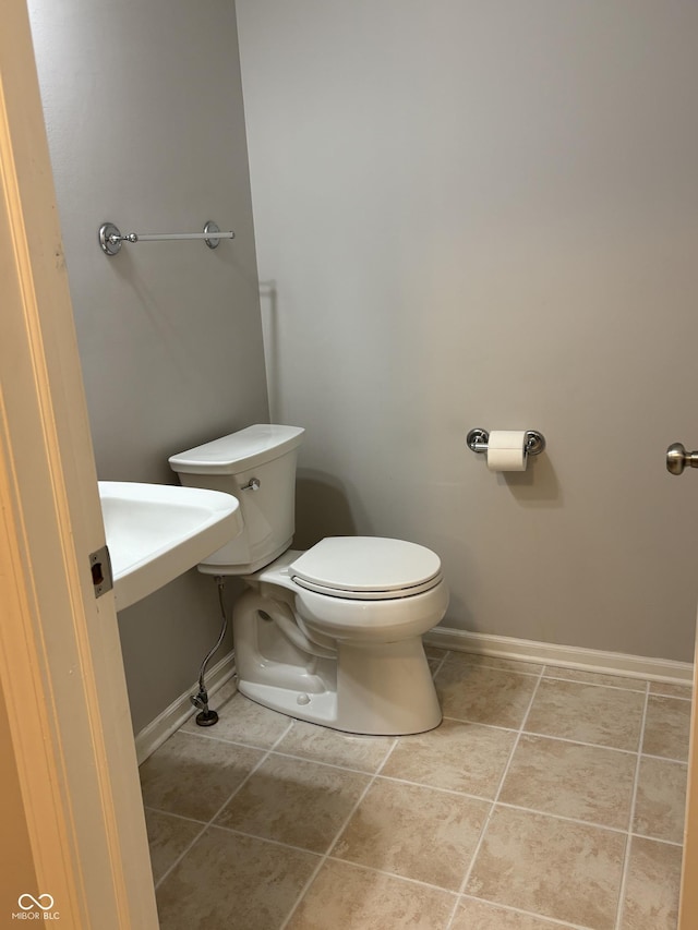 half bath featuring tile patterned flooring, toilet, and baseboards