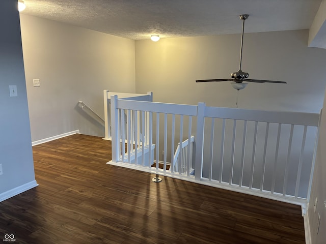 corridor with wood finished floors, an upstairs landing, baseboards, and a textured ceiling