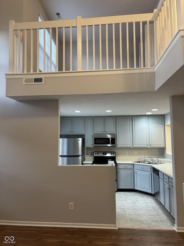 kitchen featuring gray cabinetry, light countertops, a high ceiling, stainless steel appliances, and a sink