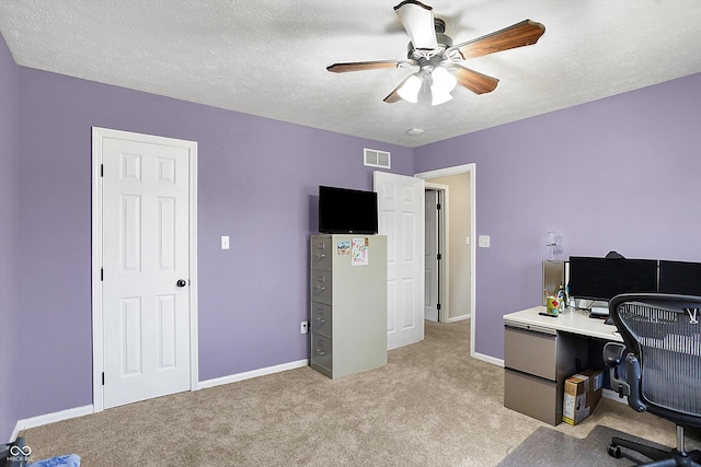 office space with visible vents, a ceiling fan, a textured ceiling, baseboards, and light colored carpet