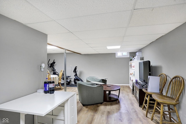 living room with a drop ceiling, baseboards, and light wood-style floors