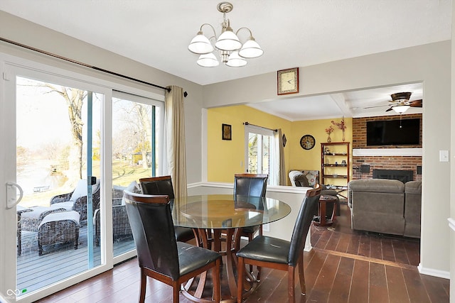 dining area featuring ceiling fan with notable chandelier, dark wood-type flooring, and a fireplace