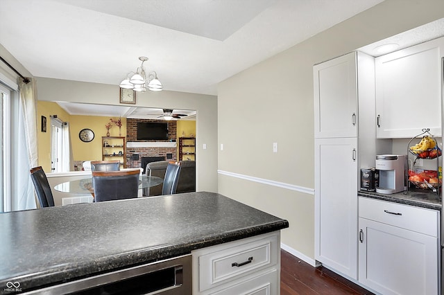 kitchen with ceiling fan with notable chandelier, dark countertops, dark wood-style floors, white cabinets, and a fireplace