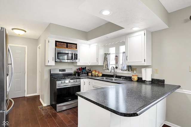 kitchen with a peninsula, a sink, stainless steel appliances, white cabinetry, and dark countertops