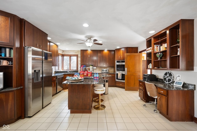 kitchen featuring open shelves, a kitchen breakfast bar, a kitchen island, built in desk, and appliances with stainless steel finishes