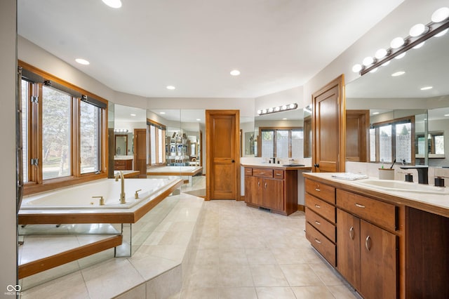 bathroom featuring a bath, two vanities, a wealth of natural light, and a sink