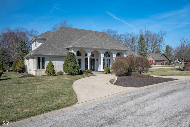 view of front of property with a front yard, driveway, roof with shingles, covered porch, and brick siding