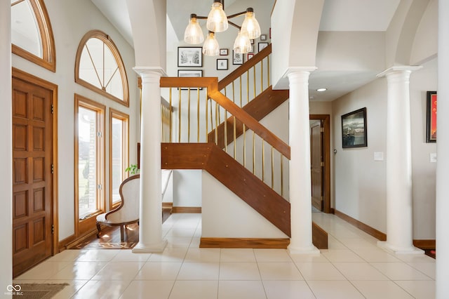 entryway with tile patterned floors, baseboards, a high ceiling, and ornate columns