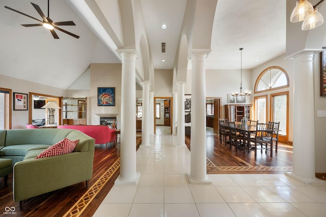 entryway featuring tile patterned floors, decorative columns, high vaulted ceiling, and a glass covered fireplace