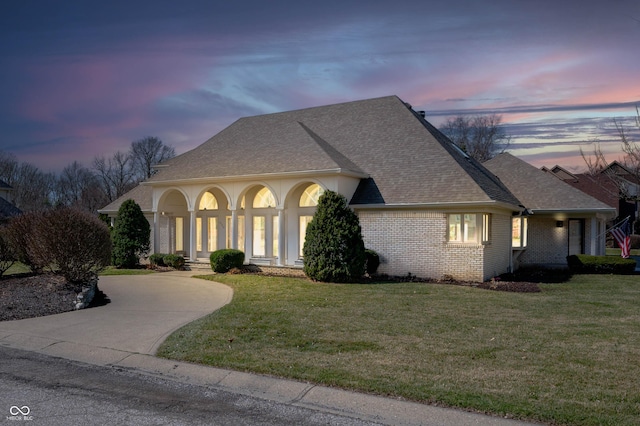 view of front of home featuring brick siding, driveway, a front lawn, and roof with shingles