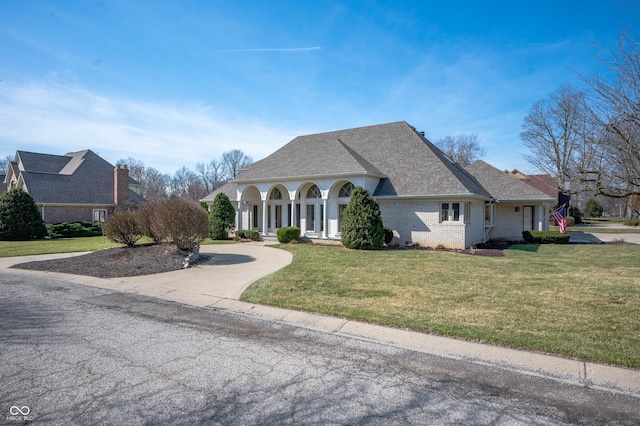 view of front of house with a front lawn, concrete driveway, brick siding, and roof with shingles